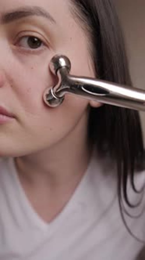 Schönheitsroutine am Morgen: Gesichtsmassage mit einer Metallrolle für einen verbesserten Hautton, Lifting-Effekt,