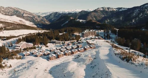 Beautiful Aerial Panorama of Winter Holiday Resort Chalet Houses and Snowy Ski Trail Slope with