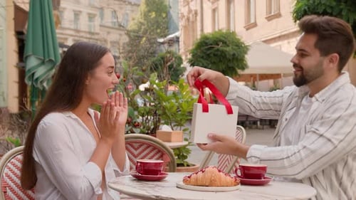 Woman Receives Gift From Man at Outdoor Cafe