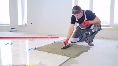 Man Carefully Installing Tile Flooring in Bright Room