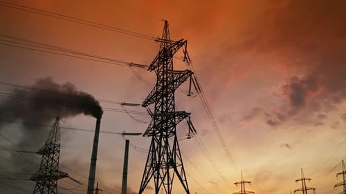 Electric towers near factory chimney with dark smoke.