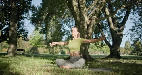 Young Beautiful White Girl Doing Yoga in Park Among Trees in Clearing on Summer Day