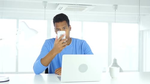 AfroAmerican Man Using Smartphone Browsing Online at Work