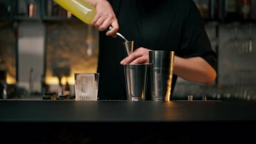 Male Bartender Hands Holding Bottle and Masterfully Pours Beverage Into Steel Jigger