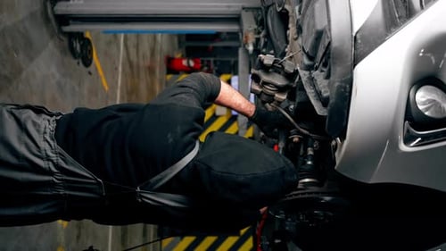 Vertical Video an Auto Mechanic at a Service Station Unscrews the Bolts Under the Body with a Wrench