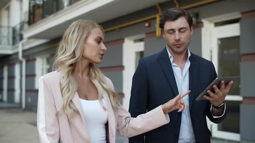 Serious business couple discussing project on tablet computer walking at city street