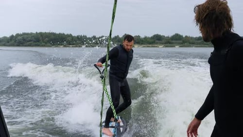 Man wakesurfing with friend watching on lake