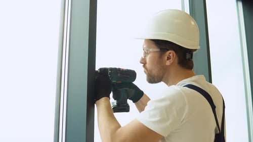 A Repairman in Uniform with Electric Screwdriver Fixing Pvc Windows in New Office