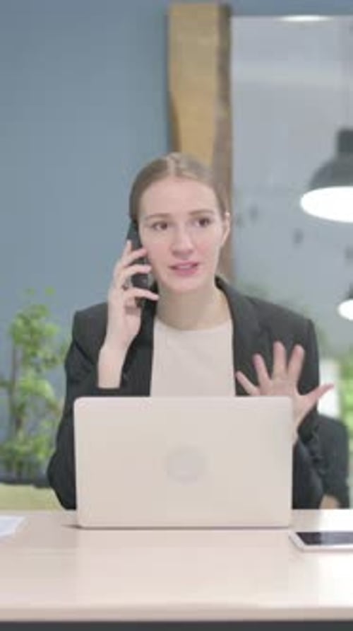 Young Woman Talking on Smartphone at Desk