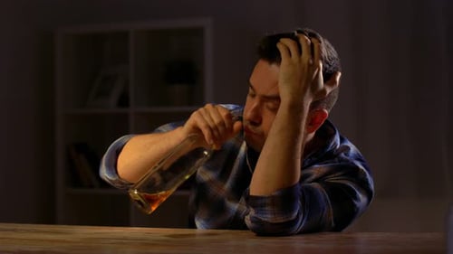 Distressed Man Drinks from a Bottle at Table