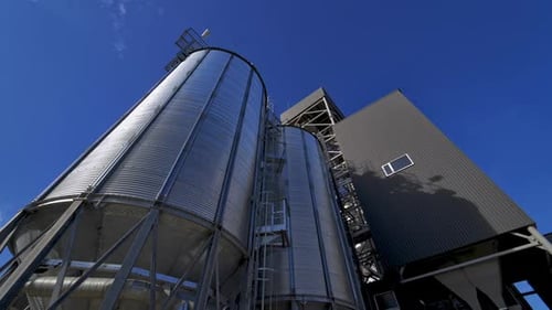 Silver containers outside. Modern agricultural complex against blue sky. Large grain elevators.