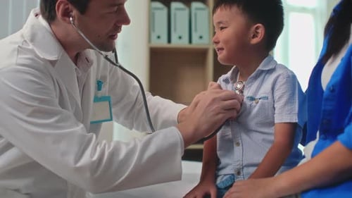 Small Cheerful Boy Looking at Doctor Listening to His Chest
