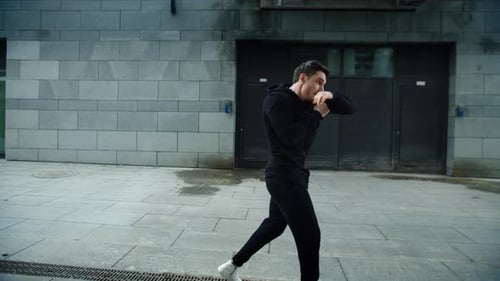 Man shadow boxing outdoors on grey city street