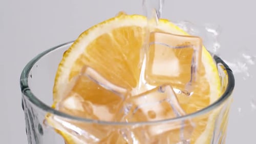 Pouring Water into Glass with Lemon and Ice