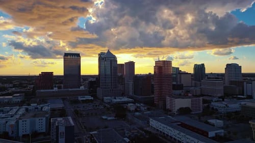 Horizonte de Tampa ao entardecer com nuvens dramáticos e reflexos de luz quente no vidro, rastreamento aéreo até