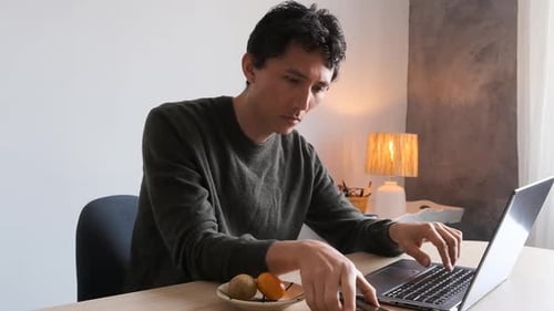 Man Works At Laptop, Uses Smartphone at Desk