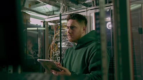 Hacker or engineer in data center holding tablet steals software or checks information from server