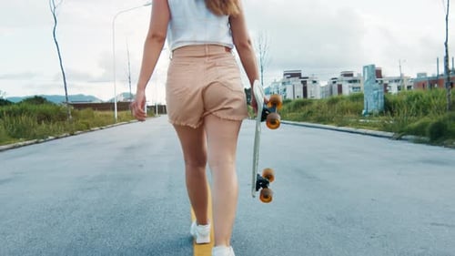 Woman walks with skateboard in her hand on the asphalt road