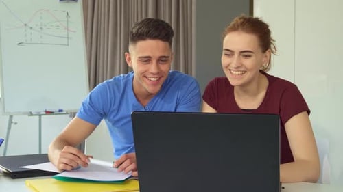 Young Couple Joyfully Collaborating on a Laptop in a Modern Office