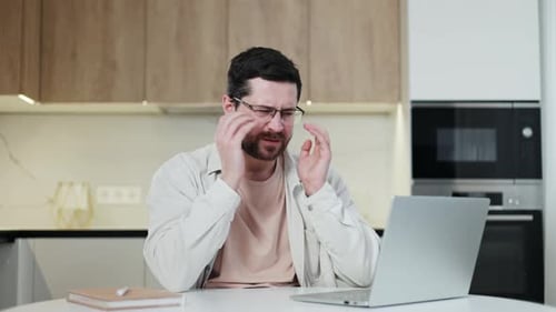 Man with Headache Working on Laptop in Kitchen