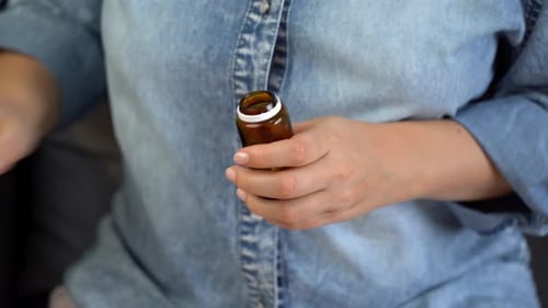 Woman opening prescription bottle, pouring pills into hand