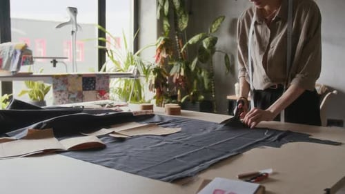 Female Tailor Cutting Black Cloth with Scissors in Studio