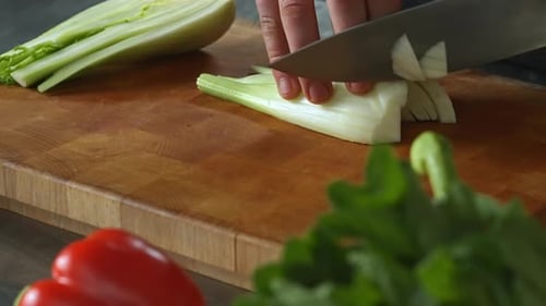 Chef carefully chopping fennel,left hand,wooden board,vegetables.