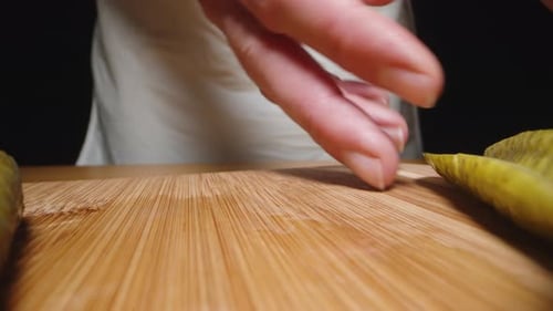 The woman slides the sliced pickles to the side of the cutting board as the camera moves backward