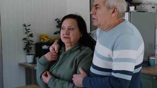 Senior Couple Embracing and Looking Out Window at Home
