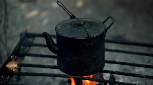 A Black Tourist Kettle Sits On A Grate Over A Fire
