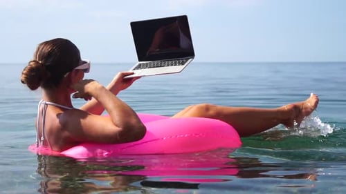 Woman Freelancer Works on Laptop Swimming in Sea on Pink Inflatable Ring Happy Tourist in Sunglasses