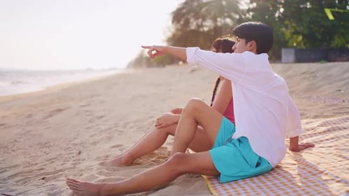 Asian young couple having picnic on the beach during summer together.