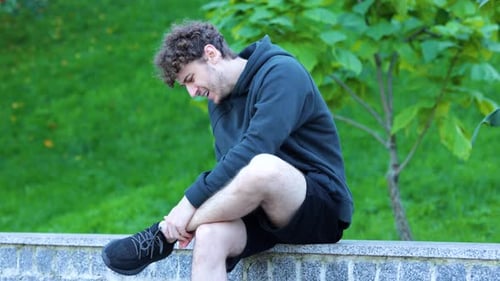 Caucasian Man Sitting and Massaging His Leg in Green Park Sportsman Feeling Strong Pain in His Ankle