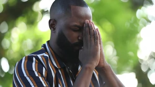 Man with Beard Praying Outdoors in Green Setting
