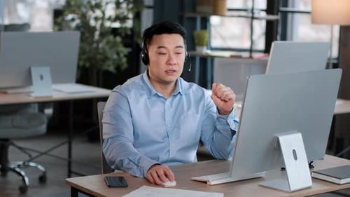 Asiatischer Mann mittleren Alters mit Headset, der mit dem Kunden spricht und am Computer tippt, um das Problem zu lösen