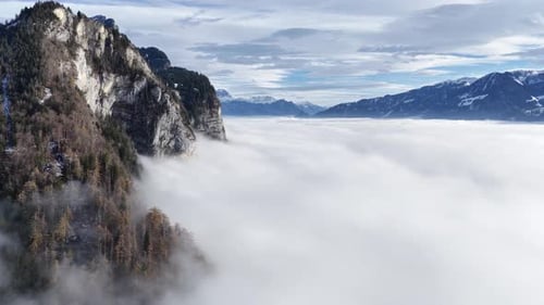aerial - rugged cliffside emerging over a bright rolling cloud ocean in churfirsten