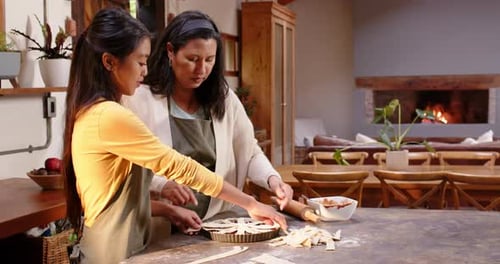 Multiracial grandmother and granddaughter preparing pie together in cozy kitchen, at home