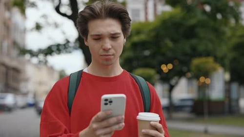 Young Adult Walking with Coffee Looking at Phone