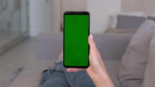 A Woman Makes a Swipe Right Gesture on a Green Smartphone Screen While Lying on the Sofa at Home