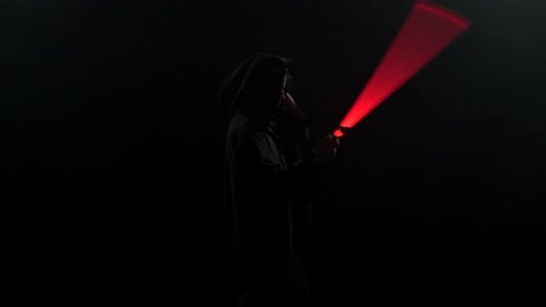 Young Man in Jedi Cosplay Costume with Lightsaber Battle on Black Background in Smoke and Rain Slow