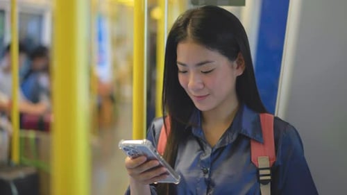 Asian woman using smartphone, stand leaning on the pole, woman in subway metro