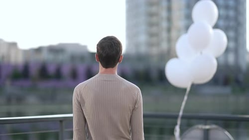 Man with Balloons Stands on Balcony, Arms Raised