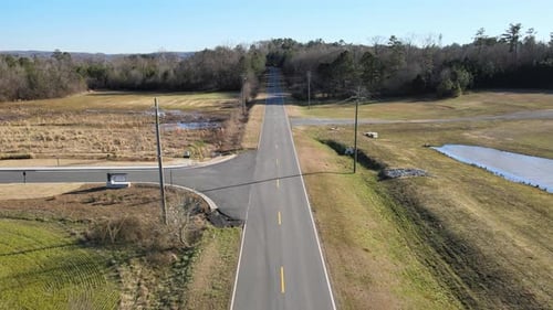Traveling down a rural two lane road with vehicles passing by. Small town setting with homes, trees,