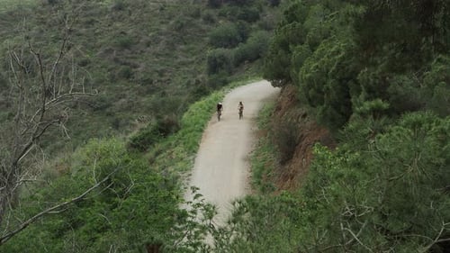 Wide Shot of Two Unrecognizable Cyclists Pedaling Along a Path in a Mountain