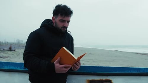 Der Mann liest vorsichtig ein Buch, während er im Winter am Meer entspannt