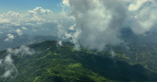 Flying trough white fluffy clouds above green mountain peaks. Beautiful summer sunny day on the high