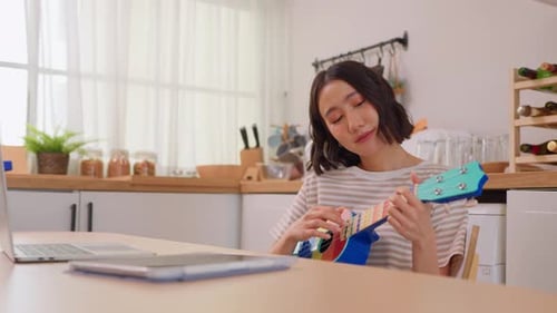 Woman Plays Ukulele at Kitchen Table