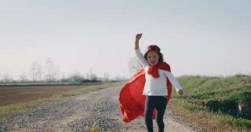 Authentic shot of a funny little girl dressed as superhero in red cape running and having fun on a