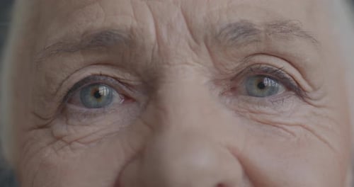 Nahaufnahme, Zeitlupenporträt der Augen einer glücklichen Seniorin, die mit Freude in die Kamera blickt