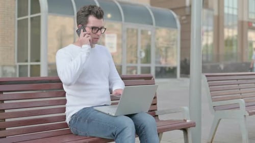 Man on Bench Talking on Phone Using Laptop